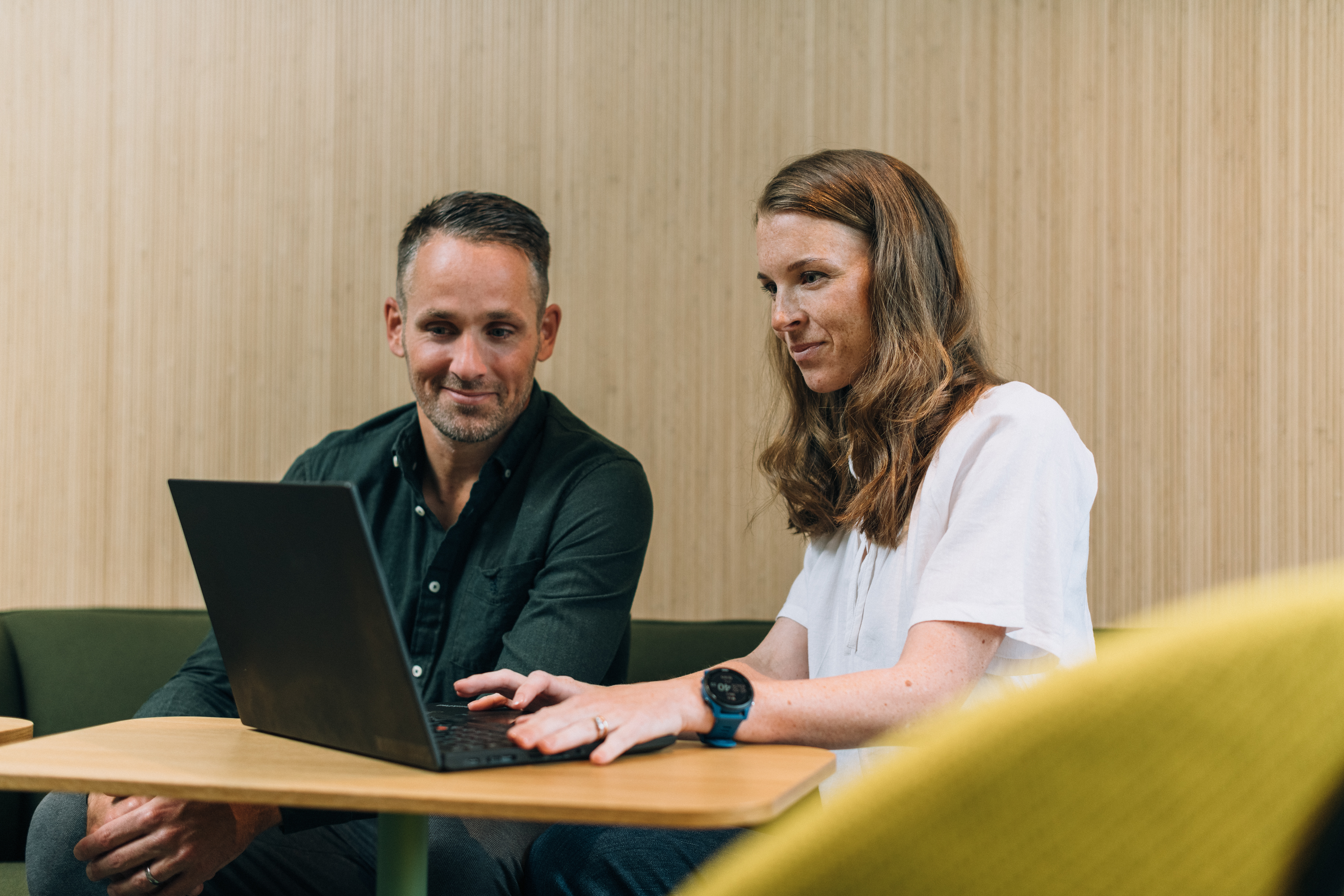 Två personer sitter vid ett bord med en bärbar dator och samarbetar kring en uppgift.