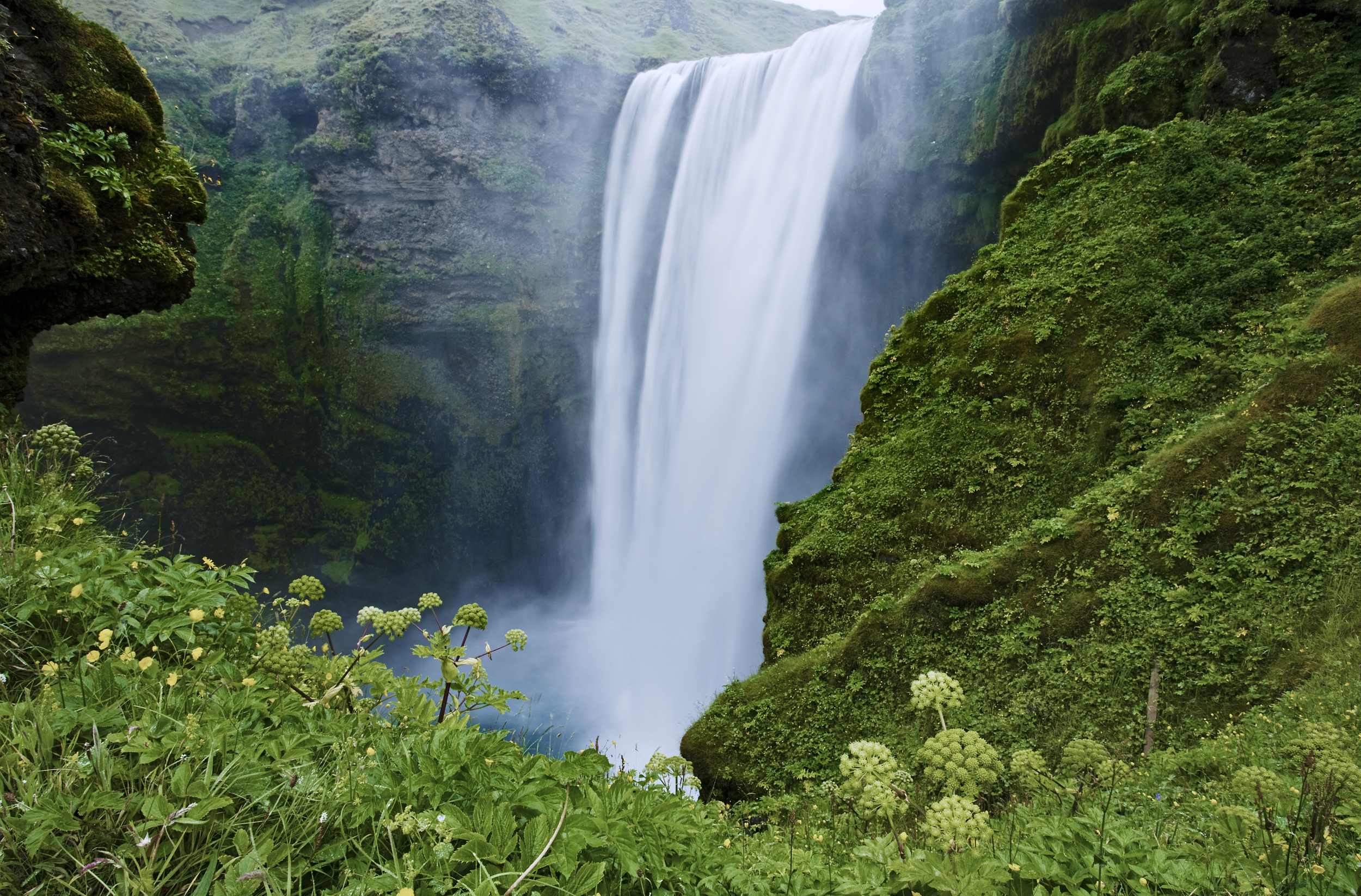 Stort vattenfall omgivet av frodig grönska, som rinner ner i en dimmig bassäng.